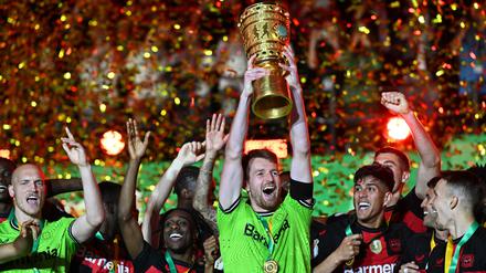 Leverkusens Torhüter Lukas Hradecky (M) hält den Pokal jubelnd hoch während seine Teamkollegen feiern.