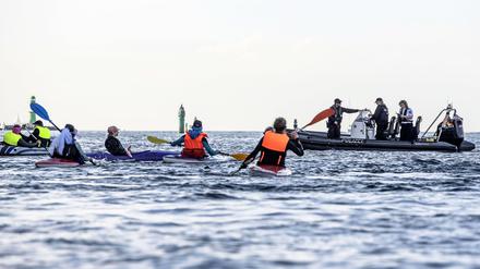 Klimaaktivist:innen versuchen auf Kanus und aufblasbaren Booten das Kreuzfahrtschiff „Aida Diva“ am Auslaufen zu hindern, während Polizeiboote in das Geschehen eingreifen. Die Aktivist:innen haben eine Aktion gegen den Kreuzfahrttourismus gestartet.