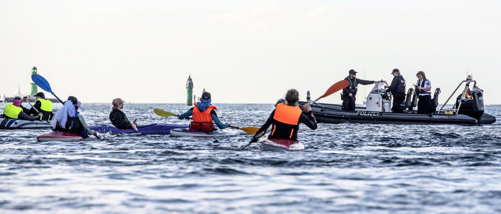 Klimaaktivist:innen versuchen auf Kanus und aufblasbaren Booten das Kreuzfahrtschiff „Aida Diva“ am Auslaufen zu hindern, während Polizeiboote in das Geschehen eingreifen. Die Aktivist:innen haben eine Aktion gegen den Kreuzfahrttourismus gestartet.