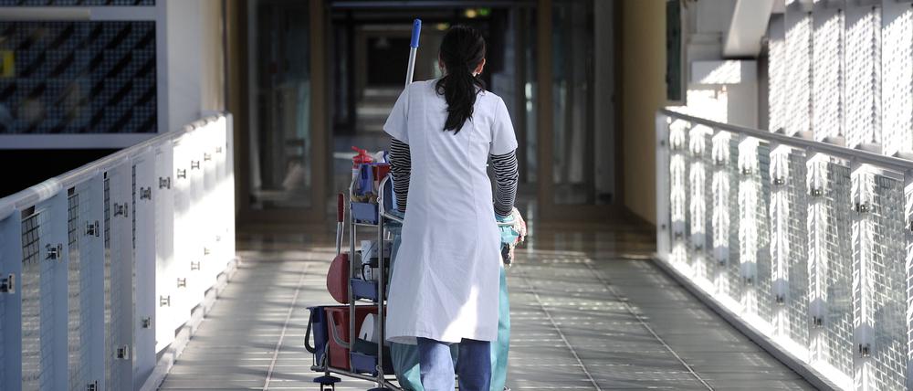 Eine Putzkraft schiebt einen Wagen durch ein Krankenhaus.