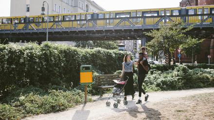 Young man carrying daughter on shoulders while woman pushing baby stroller at footpath against railway bridge