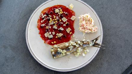 Matjes mit Zwiebeln auf einem Teller, daneben Krebssalat und Carpaccio mit Käse und Pinienkernen.