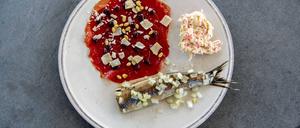Matjes mit Zwiebeln auf einem Teller, daneben Krebssalat und Carpaccio mit Käse und Pinienkernen.