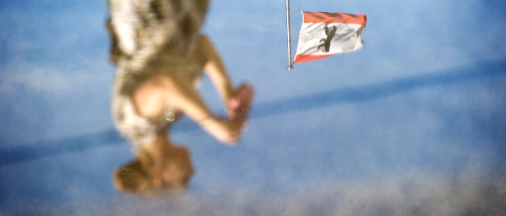 dpatopbilder Die Berliner Flagge auf dem Abgeordnetenhaus spiegelt sich am 12.08.2014 in in einer Pfütze in Berlin gemeinsam mit einer Frau, die ein Foto aufnimmt. Foto: Daniel Naupold/dpa ++ +++ dpa-Bildfunk +++