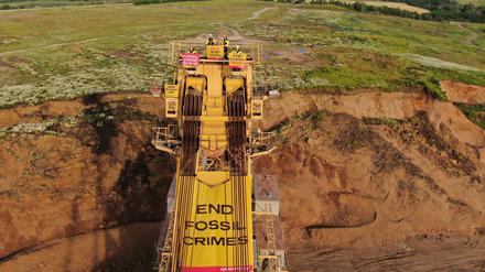 Aktivisten aus Tschechien, Polen und Deutschland stehen auf einem Schaufelradbagger und halten dabei Transparente mit der Aufschrift „End Fossil Crimes“ und „End Mining 2030“.