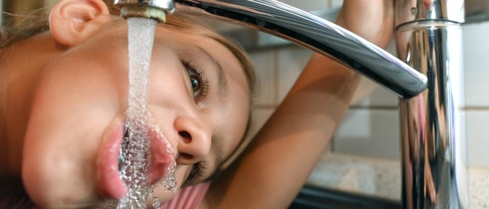 Ein Mädchen trinkt Leitungswasser aus einem Wasserhahn.