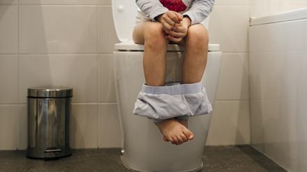 Close up of young Caucasian girls legs sat on the toilet in the bathroom with her pyjama pants round her ankles.