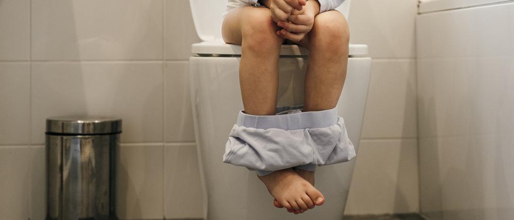 Close up of young Caucasian girls legs sat on the toilet in the bathroom with her pyjama pants round her ankles.