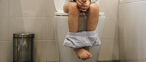 Close up of young Caucasian girls legs sat on the toilet in the bathroom with her pyjama pants round her ankles.