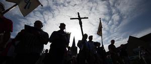 Pilger der 166. Telgter Wallfahrt gehen im Gegenlicht auf einer Straße und halten ein Kreuz.