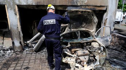 Ein Polizist untersucht ein bei den Krawallen ausgebranntes Auto.