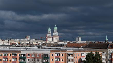 Die beiden Wohntürme am Frankfurter Tor sind über den Dächern von Wohn- und Geschäftshäusern im Stadtteil Friedrichshain vor dunklen Wolken zu sehen.