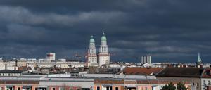 Die beiden Wohntürme am Frankfurter Tor sind über den Dächern von Wohn- und Geschäftshäusern im Stadtteil Friedrichshain vor dunklen Wolken zu sehen.