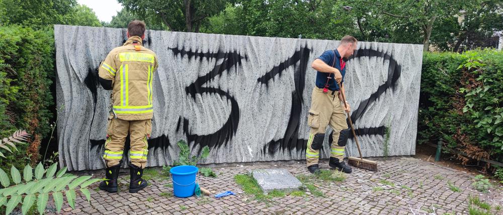 Feuerwehr-Männer versuchen, das Ehrenmal am Mariannenplatz zu reinigen