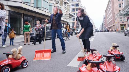 Ein Demonstrant mit einer Kai-Wegner-Maske und eine Demonstrantin mit Manja-Schreiner-Maske kehren symbolisch auf der Friedrichstraße die Bobbycars aus dem Weg.