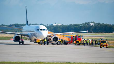 Feuerwehrfahrzeuge und Einsatzkräfte stehen neben dem auf dem Flugfeld abgestellten Flugzeug.