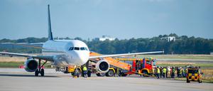 Feuerwehrfahrzeuge und Einsatzkräfte stehen neben dem auf dem Flugfeld abgestellten Flugzeug.