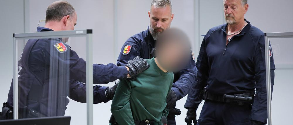 Der Angeklagte wird von Justizbeamten an seinen Platz im Gerichtssaal gebracht.