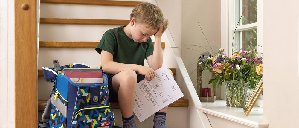 Ein enttäuschter Junge sitzt zu Hause mit seinem schlechten Zeugnis aus der Grundschule auf der Treppe.