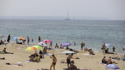 08.07.2023, Spanien, Palma: Menschen sonnen sich und benutzen Sonnenschirme am Strand Can Pere Antoni in Palma während der Hitzewelle.