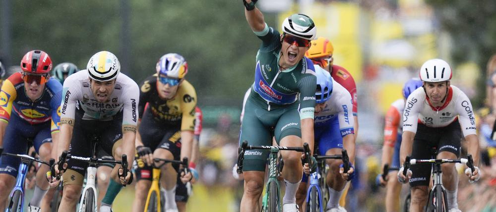 Jasper Philipsen (M) aus Belgien vom Team Alpecin-Deceuninck zeigt vier Finger, während er vor dem Drittplatzierten Phil Bauhaus (2.v.l.) aus Deutschland vom Team Bahrain Victorious als Etappensieger über die Ziellinie fährt.