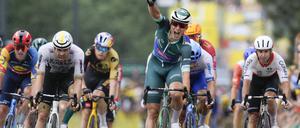 Jasper Philipsen (M) aus Belgien vom Team Alpecin-Deceuninck zeigt vier Finger, während er vor dem Drittplatzierten Phil Bauhaus (2.v.l.) aus Deutschland vom Team Bahrain Victorious als Etappensieger über die Ziellinie fährt. 