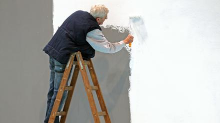 Ein älterer Herr mit grauen Haaren weißt eine Wand.