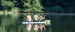 Drei Jungen sitzen mit Angelruten auf einem SUP auf einem See am Cottbuser Stadtrand. 