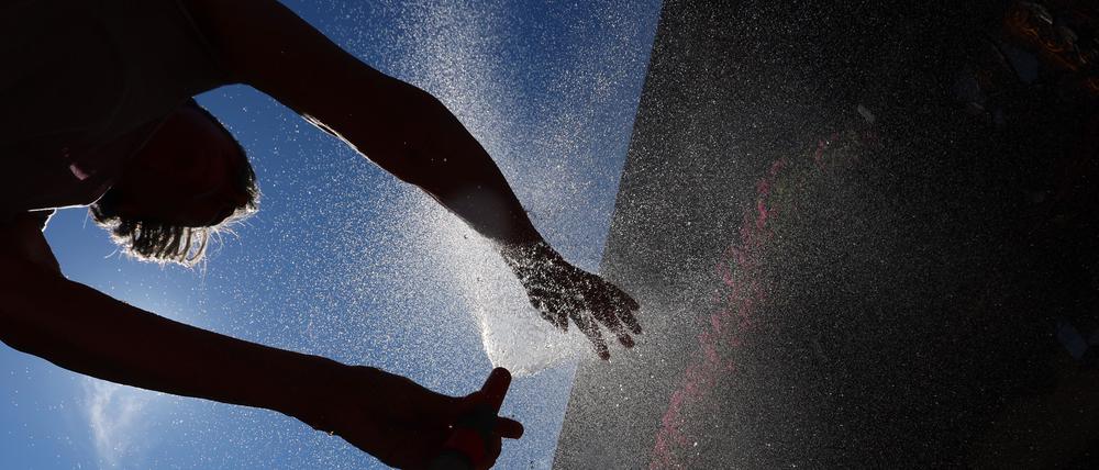 15.07.2023, Bayern, Kaufbeuren: Eine Frau kühlt sich in einem Garten mit Wasser aus einem Gartenschlauch ab.