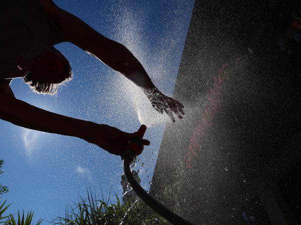 15.07.2023, Bayern, Kaufbeuren: Eine Frau kühlt sich in einem Garten mit Wasser aus einem Gartenschlauch ab.
