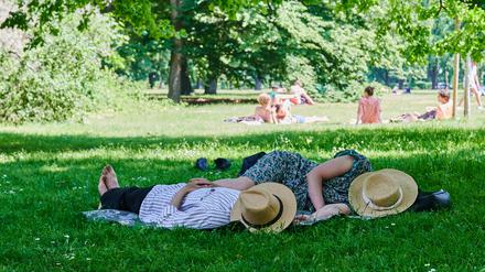 Zwei Menschen liegen mit Strohhut über dem Gesicht im Schatten eines Baumes im Berliner Tiergarten.