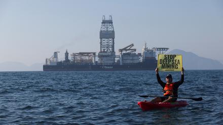 Ein Greenpeace-Aktivist hält ein Schild in die Höhe – im Hintergrund das Tiefsee-Bergbauschiff Hidden Gem (Symbolbild)