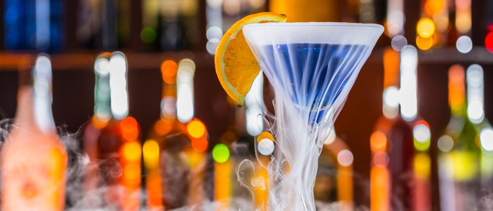Ein blauer Cocktail in einem Martiniglas steht auf einem Tresen.