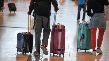 Reisende gehen im Flughafen Berlin-Brandenburg (BER) mit Koffern durch den Abflugsterminal.