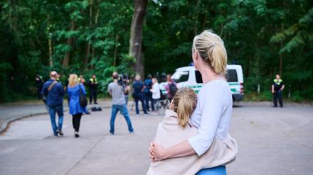 Eine Anwohnerin und ihre Tochter sehen Journalisten und Polizei zu, während Tierexperten und Polizeibeamten in einem Waldgebiet in Zehlendorf stehen. 