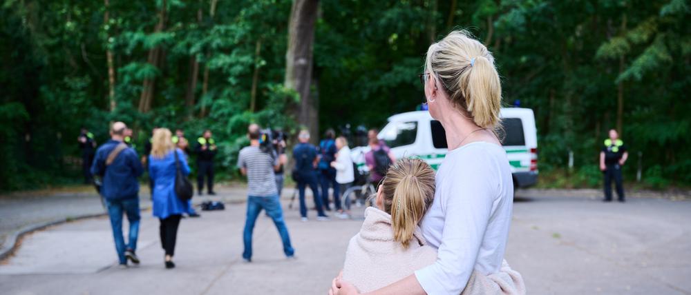 Eine Anwohnerin und ihre Tochter sehen Journalisten und Polizei zu, während Tierexperten und Polizeibeamten in einem Waldgebiet in Zehlendorf stehen.