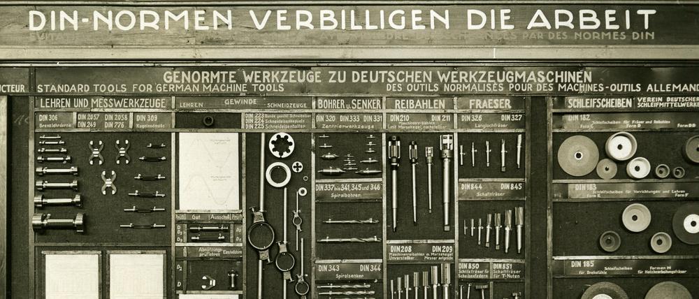 Präsentation von genormten Werkzeugen und dem Slogan „DIN Normen verbilligen die Arbeit“. Das Datum der Aufnahme ist nicht bekannt.