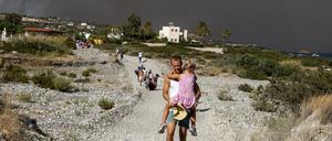 Ein Mann trägt ein Kind, als sie ein Waldbrandgebiet verlassen. 