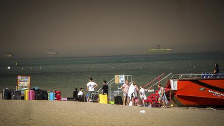 22.07.2023, Griechenland, Rhodos: Touristen stehen an einem Strand, wohin sie wegen eines Waldbrandes auf der griechischen Insel Rhodos in Sicherheit gebracht worden sind. Ein großer Brand auf der griechischen Insel Rhodos, der bereits den fünften Tag andauert, hat die Behörden gezwungen, die Evakuierung von vier Orten anzuordnen, darunter zwei Badeorte. Foto: Argyris Mantikos/Eurokinissi/AP/dpa +++ dpa-Bildfunk +++