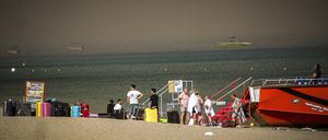 22.07.2023, Griechenland, Rhodos: Touristen stehen an einem Strand, wohin sie wegen eines Waldbrandes auf der griechischen Insel Rhodos in Sicherheit gebracht worden sind. Ein großer Brand auf der griechischen Insel Rhodos, der bereits den fünften Tag andauert, hat die Behörden gezwungen, die Evakuierung von vier Orten anzuordnen, darunter zwei Badeorte. Foto: Argyris Mantikos/Eurokinissi/AP/dpa +++ dpa-Bildfunk +++