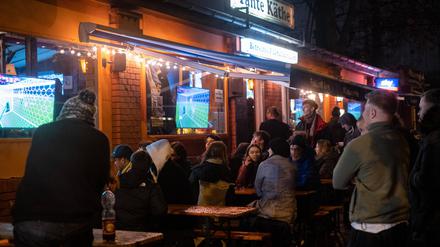 Fußballfans verfolgen das Spiel Deutschland gegen Costa Rica anlässlich Fifa Fußball-Weltmeisterachaft 2022 bei nassen und kaltem Wetter vor der Fußballbar Tante Käthe in Berlin-Prenzlauer Berg.
