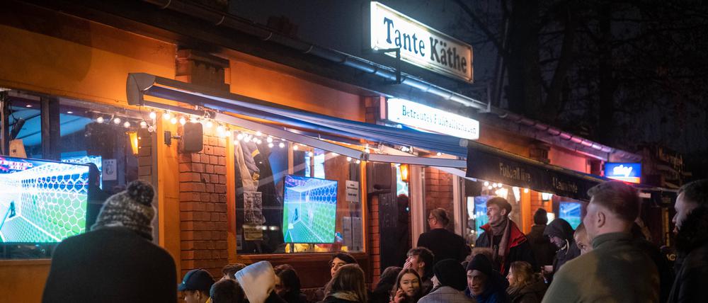 Fußballfans verfolgen das Spiel Deutschland gegen Costa Rica anlässlich Fifa Fußball-Weltmeisterachaft 2022 bei nassen und kaltem Wetter vor der Fußballbar Tante Käthe in Berlin-Prenzlauer Berg.