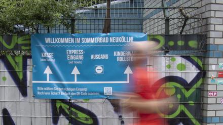 Eine Person geht an einem Transparent vorbei, das an einem Zaun vom Columbiabad in Neukölln als Wegweiser hängt. Nach der Debatte über Jugendgewalt in Berliner Freibädern vor einigen Wochen hat sich die Lage nach Einschätzung der Polizei entspannt. 