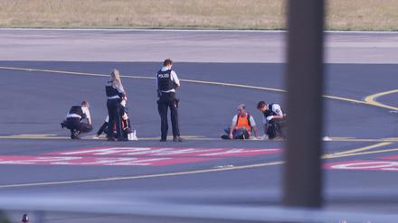Polizisten stehen im Sommer auf dem Flugfeld Düsseldorf und versuchen Aktivisten der Gruppe „Letzte Generation“ vom Asphalt zu lösen.