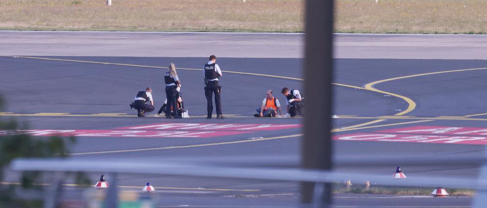Polizisten stehen im Sommer auf dem Flugfeld Düsseldorf und versuchen Aktivisten der Gruppe „Letzte Generation“ vom Asphalt zu lösen.