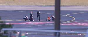 Polizisten stehen im Sommer auf dem Flugfeld Düsseldorf und versuchen Aktivisten der Gruppe „Letzte Generation“ vom Asphalt zu lösen.