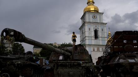 Ein Junge steht auf einem zerstörten russischen Panzer, der vor den goldenen Kuppeln des Klosters St. Michael 