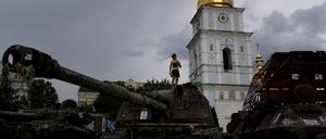 Ein Junge steht auf einem zerstörten russischen Panzer, der vor den goldenen Kuppeln des Klosters St. Michael 