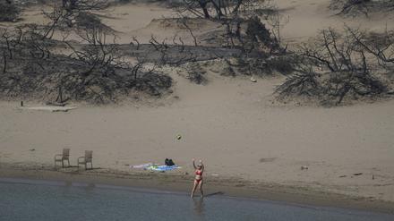 Eine Frau spielt mit einem Ball vor einem verbrannten Wald an einem Strand auf Rhodos.