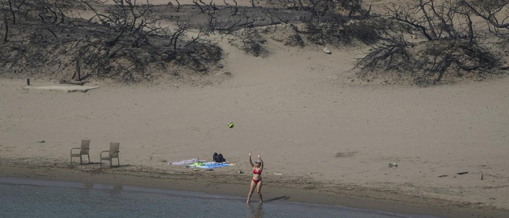 Eine Frau spielt mit einem Ball vor einem verbrannten Wald an einem Strand auf Rhodos.